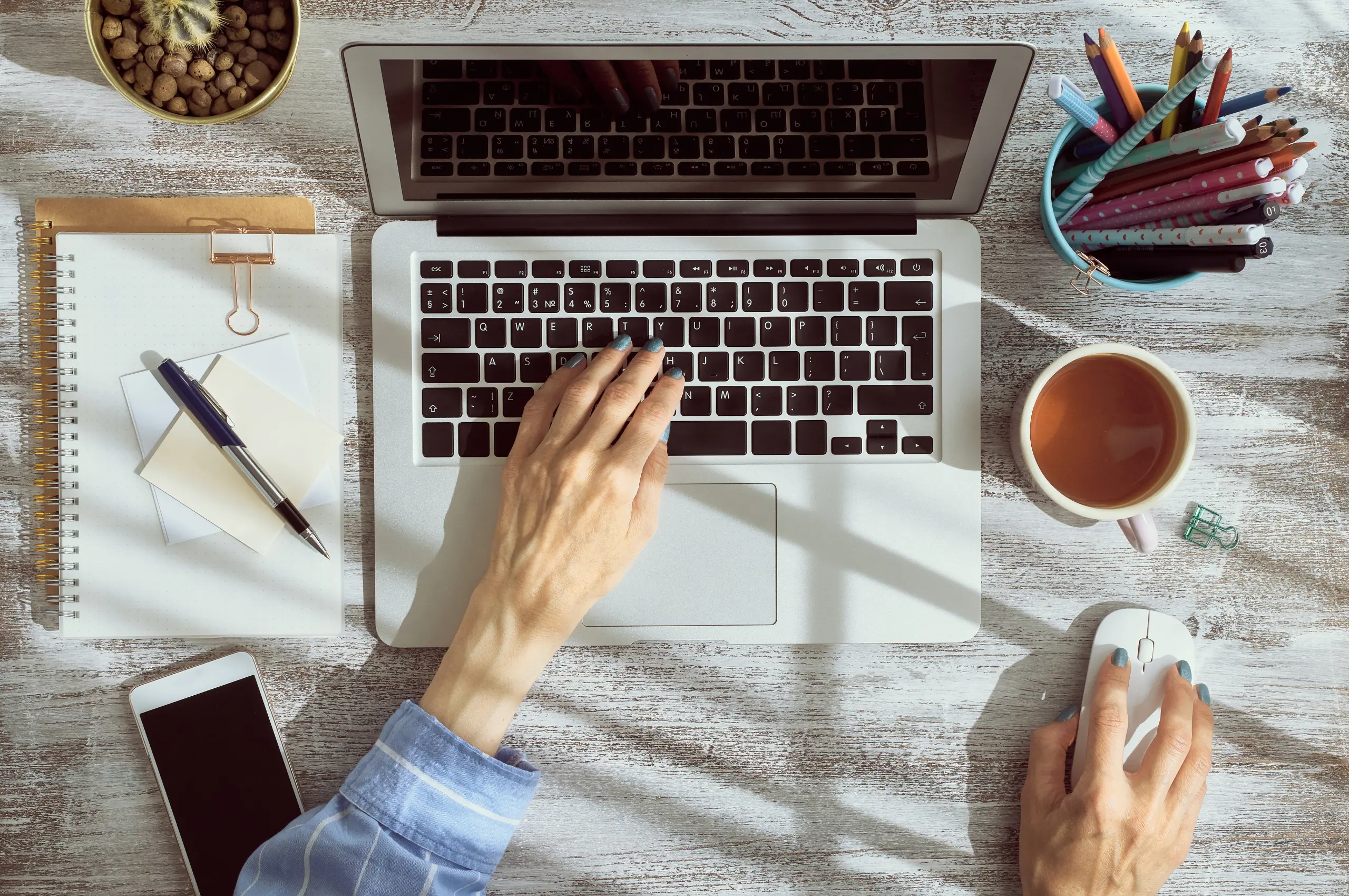 flatlay with woman's hand over a macbook in a, a coffee and some other desk elements